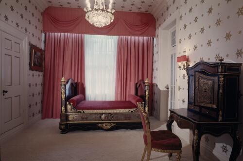 [Wooden bed with ormolu posts and red and gold fabrics in a room with white wallpaper with a gold pattern and a cabinet and chair in the foreground, ca. 1971] [transparency] / David Beal