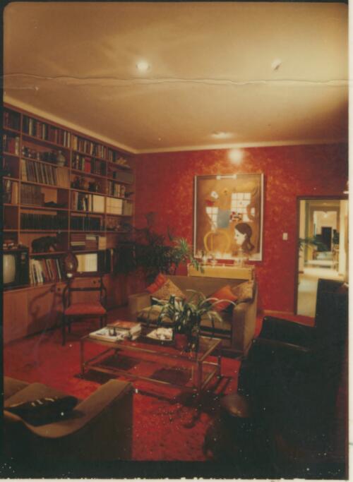 Living room with tomato red carpet, red flocked wallpaper, shiny gold ceiling and a wall of shelves housing books and a television, ca. 1971 [picture] / David Beal