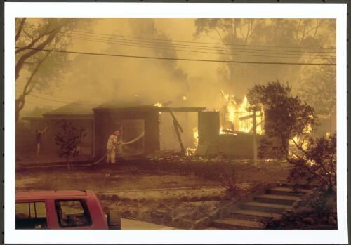 Bushfire fighters from Belrose in Sydney and a neighbour working to prevent fire spreading from this gutted house to the neighbouring property in Kambah, [18 January 2003] [picture] : / Jeff Cutting