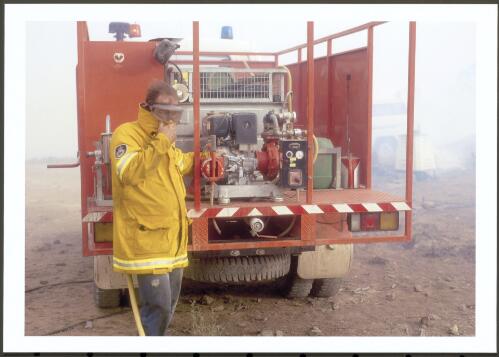Peering out into a scorching gritty wind, the pump operator on a Monaro District tanker winces as he strains to keep sight of his nozzle man, [30 January 2003] [picture] / Jeff Cutting