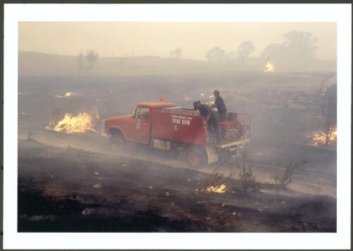A vintage bushfire tanker from the Monaro district outrun by the fast moving spot fires withdraws to work the flanks and mop up burning material, Clear View Range Road, Michelago, 30 January 2003 [picture] / Jeff Cutting