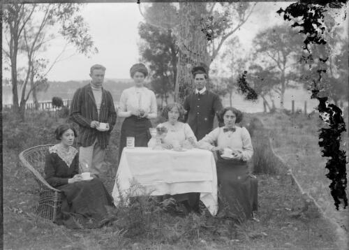 Group around outdoor table, possibly having afternoon tea? [picture] / C.C. Fox