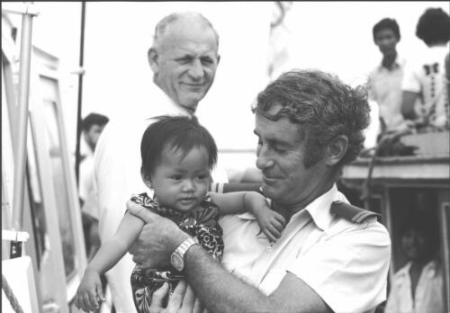 Customs officer Frank Dalton holding a Vietnamese refugee child, Xye Than Hue, Darwin, November 1977 [picture] / Michael Jensen