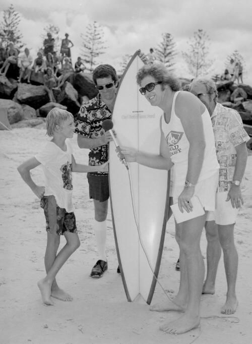 4GG announcer Darrell Eastlake with Ross Thompson on right interviewing a young surfer during the Sand Modelling and Surf Contest events sponsored by 4GG and Carl Robertson Ford of Southport and held on Burleigh Heads beach, Queensland, 3 February 1974 [picture] / Ray Sharpe