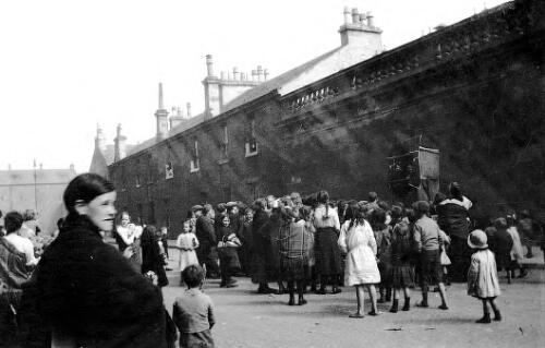 Street scene, children watching Punch and Judy show, Gullane Street, Partick, Glasgow, Scotland, ca. 1918, 1 [picture] / Rex Nan Kivell