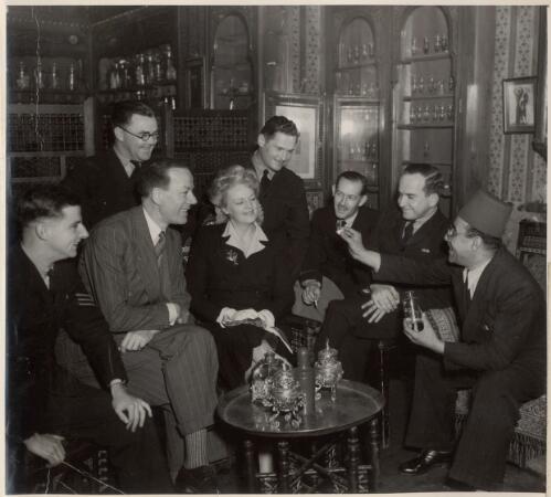 [Cyril Ritchard and Madge Elliott being shown an item from a glass container by a man, with five servicemen looking on] [picture]