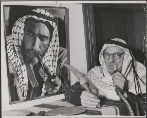 Frank Hurley in "Lawrence of Arabia Costume" beside a portrait of Sheikh Jirwan Mijali [picture]