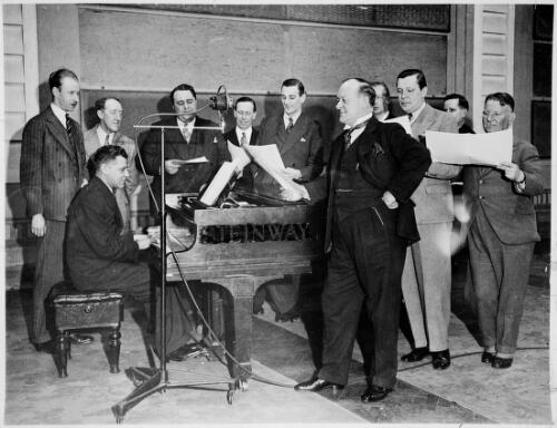 Portait of Peter Dawson, vocalist, leaning on piano, with Ray Noble, George Baker, Webster Booth, an unidentified pianist and seven unidentified men, ca. 1933 [picture]