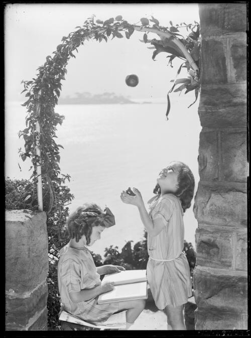 Adelie Hurley, reading, and Toni Hurley, pretending to catch an orange, at Stonehenge, Rose Bay, Sydney, ca. 1927 [picture] / Frank Hurley