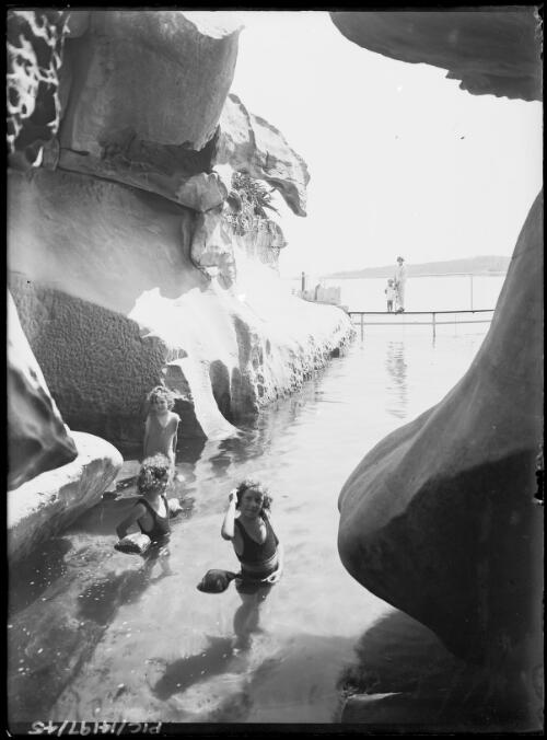 Yvonne, rear left, Adelie, left, and Toni Hurley at the natural swimming pool, with Frank Junior and Antoinette Hurley on the bridge in the background, Point Piper, Sydney, ca. 1927 [picture] / Frank Hurley