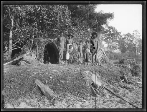 Aboriginal family standing outside their shelter on an embankment, Northern Australia, approximately 1914/ Frank Hurley