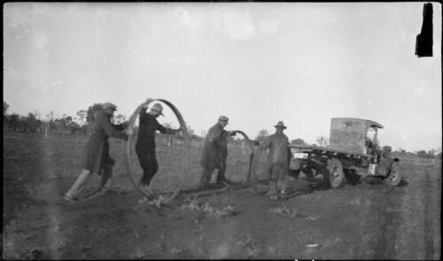Four men push two large steel hoops to a truck in a field, Bourke, New South Wales, 26 April 1929 [picture]