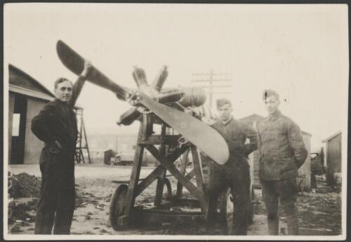 Three soldiers standing next to an aircraft engine mounted on a trolley, England, 1917 [picture] / John Joshua
