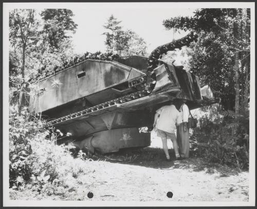 Two men inspecting the underside of a derelict tank, surplus World War II equipment, [Noemfoor Island], Dutch New Guinea, 1953 [picture] / Thiess Bros. Pty Ltd