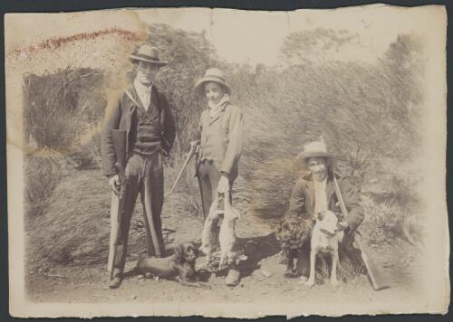 Two men carrying rifles and a youth carrying a rifle and dead rabbits, with three hunting dogs, Kalgoorlie, Western Australia, 1905? [picture]