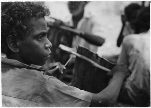 Young boy flattening a section of bark for painting, Mornington Island, Queensland, approximately 1980 / Gregory Owen