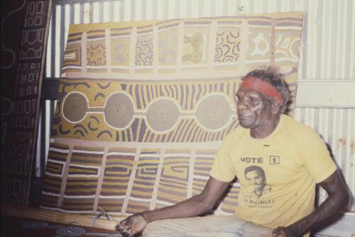 Willie Tjungarrayi seated by an artwork painted with Uta Uta Tjangala, Papunya Tula, Northern Territory, 1983 [transparency] / Andrew Crocker