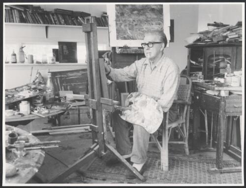 Bill Dobell seated at easel, painting with palette and brushes, Wangi Wangi, New South Wales, 1963 [picture]