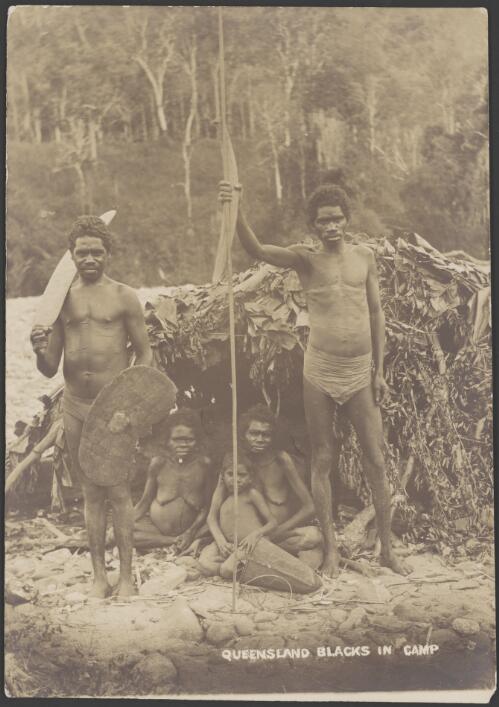 Two Aboriginal men, holding a boomerang, spear and a sword and shield, standing in front of two seated Aboriginal women and a child holding a dilly bag, Bloomfield River region [?], Queensland, ca. 1900 [picture] / Handley & Atkinson Photographers