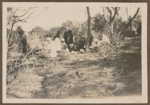 Group of people sitting amongst bushes, Koonibba Mission, South Australia