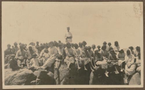 Children and staff from Koonibba Children's Home listening to a sermon, sitting on the rocks at Point James, South Australia
