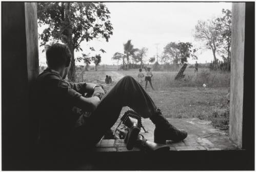 A soldier of the 1st Battalion, Royal Australian Regiment watching Vietnamese children playing near Bien Hoa, Vietnam, 1965 / Tim Page