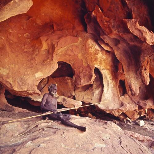 A Pitjantjatjara man sitting in a rock cave holding a spear, Uluru, Northern Territory, approximately 1966 / Robin Smith