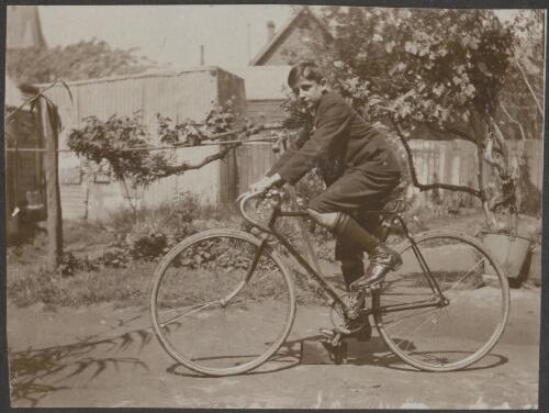 A young man riding a bicycle in a backyard, Parramatta, New South Wales / Carl Schiesser