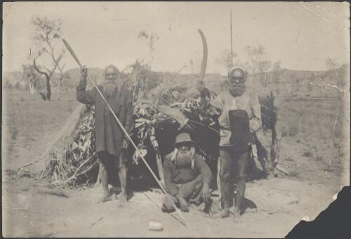 Three men in front of a wurlie, one holds a spear and another a boomerang, Northern Territory / Samuel White