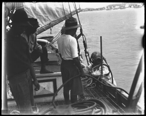 [Pearl diver beside a boat watched by three other men, Thursday Island harbour, Queensland] [picture] : [Pearling] / [Frank Hurley]