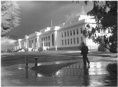 Parliament House with reflections [with figure, bubbler and bus stop 'Parliament', ca. 1938] [picture] : [Canberra, Australian Capital Territory] / [Frank Hurley]