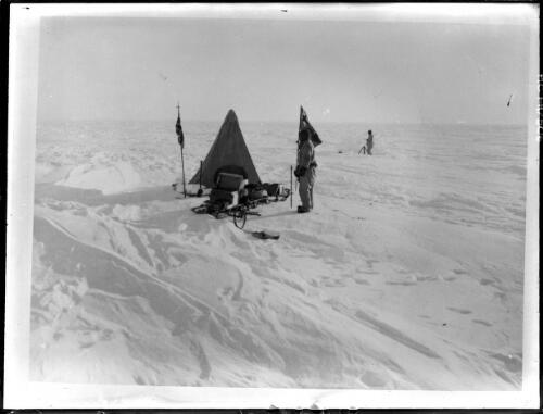 [King George V Land, farthest south camp of southern party, 17 'minutes' (about 50 miles) from the South Magnetic Pole; Edward Frederick Robert Bage near sledge, Eric Norman Webb taking set of magnetic observations behind snow barricade, Australasian Antarctic Expedition] [picture] : [Antarctica] / [Frank Hurley]