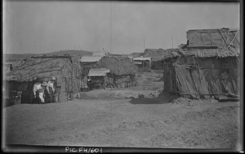 [Three women near small buildings made of wood, burlap and thatch] [picture] : [Darwin, Northern Territory] / [Frank Hurley]