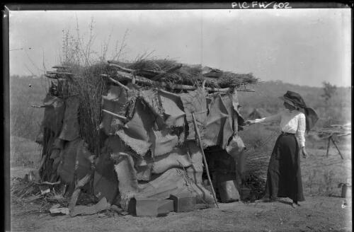 [Woman near a small building made of wood, burlap and thatch, Darwin trip with Francis Birtles? horizontal] [picture] : [Darwin, Northern Territory] / [Frank Hurley]