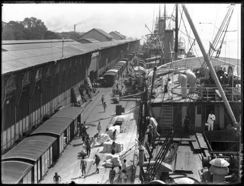 Tandjong Priok Batavia [dock with ship, workers and two women in European dress, 1913] [picture] : [Java, Indonesia] / [Frank Hurley]