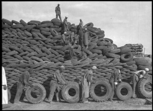 [Salvage dump, men rolling tyres and a mound of tyres] [picture] / [Frank Hurley]