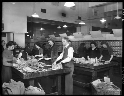 Preparing overseas airmail before sorting, sorters in background [postal workers, General Post Office, Martin Place, Sydney, 1940s] [picture] : [Sydney, New South Wales] / [Frank Hurley]