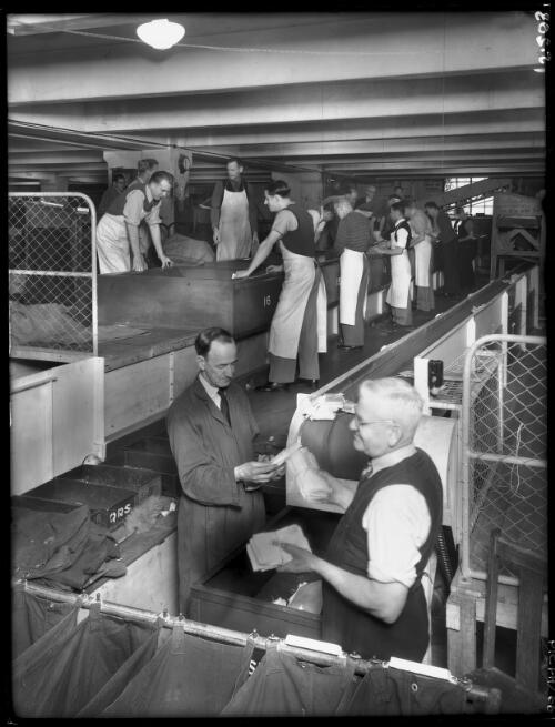 In the receiving section where bag mail is opened prior to sorting [postal workers, General Post Office, Martin Place, Sydney, ca. 1946] [picture] : [Sydney, New South Wales] / [Frank Hurley]