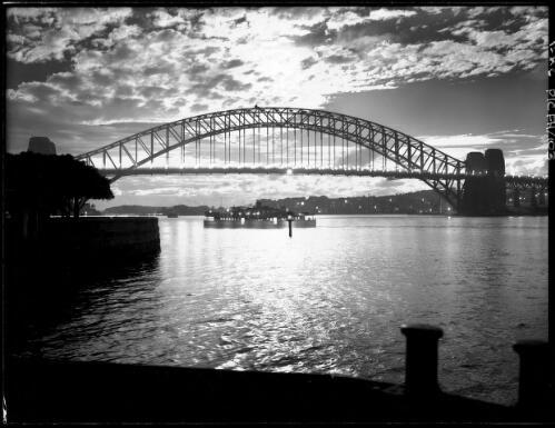 Sunset scene with lights [Sydney Harbour Bridge from South East, Royal Botanic Gardens on left] [picture] : [Sydney Harbour, New South Wales] / [Frank Hurley]