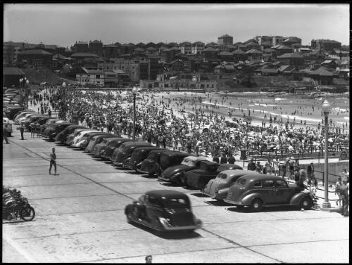 [North Bondi Beach, cars in car park, motorbikes, people, buildings] [picture] : [Beaches, Sydney, New South Wales] / [Frank Hurley]