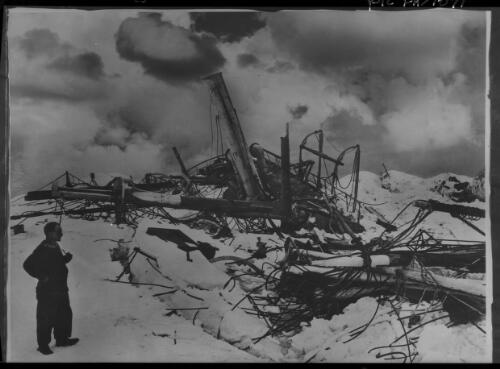 The wreckage lies scattered about in dismal confusion,  Captain Wild takes a last look at the remains of the ship  [Frank Wild with pipe and the Endurance, Shackleton expedition, 1915] [picture] : [Antarctica] / [Frank Hurley]