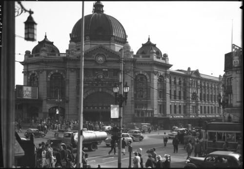 [Flinders Street Station and street intersection, with trucks, cars, a tram and people] [picture] : [Melbourne, Victoria] / [Frank Hurley]