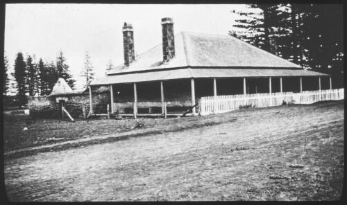 [A house with a wide verandah, two chimneys and a white picket fence] [picture] : [Norfolk Island] / [Frank Hurley]