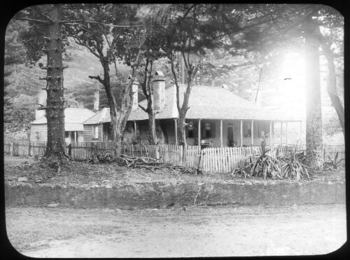 [A house with a verandah, surrounded by tall trees and a fence] [picture] : [Norfolk Island] / [Frank Hurley]
