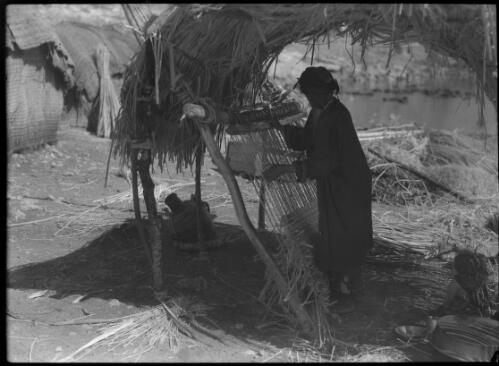 Weaving mats on primitive loom on the Shores of Lake Huleh, the material is swamp reeds [picture] / [Frank Hurley]