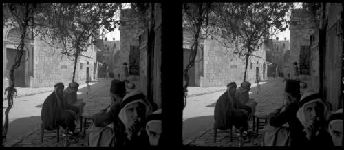 All Saints Church [a group of figures sitting on stools, talking, in a cobbled street, Jerusalem] [picture] / [Frank Hurley]