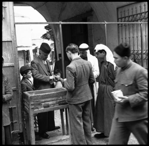 Money changer Jerusalem [with customers and two children] [picture] / [Frank Hurley]