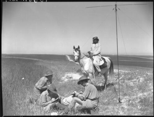 Field scene Palestine [four figures, one on horseback, three on the ground in military uniform, two writing] [picture] / [Frank Hurley]