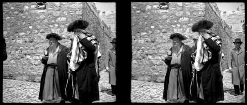 [Three figures walking in a street with high stone walls and cobbled pavement] [picture] / [Frank Hurley]