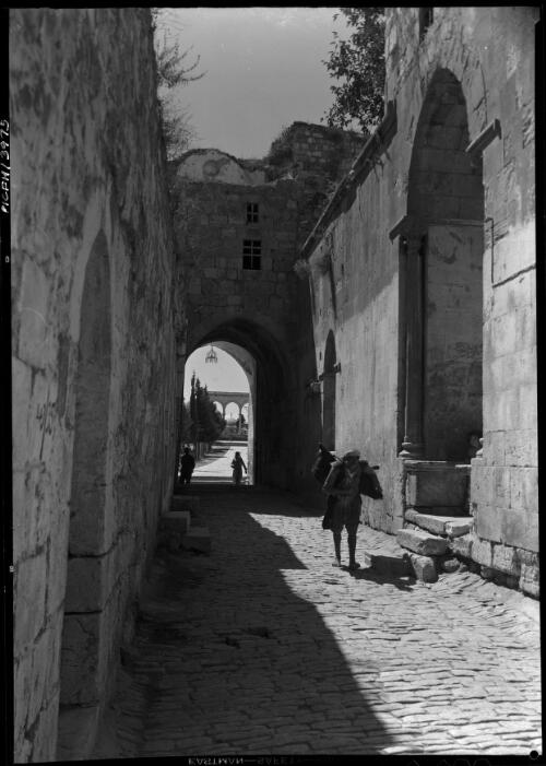 [Street scene in Jerusalem with the Dome of the Rock and Harem esh Sharif in background, and a figure walking towards the Church of the Holy Sepulchre] [picture] / [Frank Hurley]